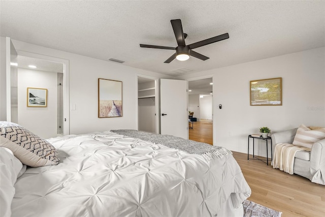 bedroom with a spacious closet, ceiling fan, light wood-type flooring, a closet, and a textured ceiling