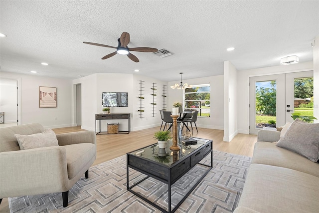 living room with a textured ceiling, ceiling fan with notable chandelier, light hardwood / wood-style floors, and french doors