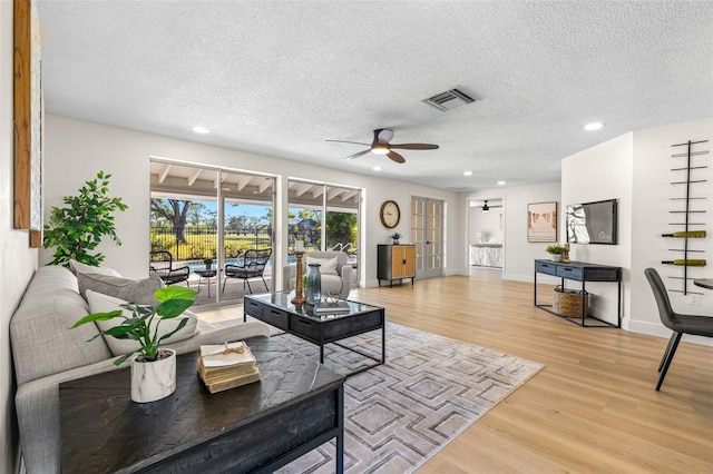 living room featuring ceiling fan, a textured ceiling, and light hardwood / wood-style flooring