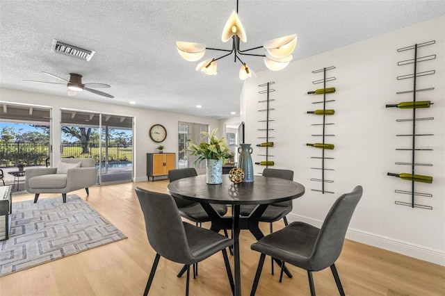 dining area with ceiling fan with notable chandelier, light hardwood / wood-style floors, and a textured ceiling