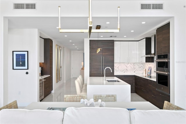 kitchen with sink, wall chimney range hood, hanging light fixtures, dark brown cabinetry, and white cabinets