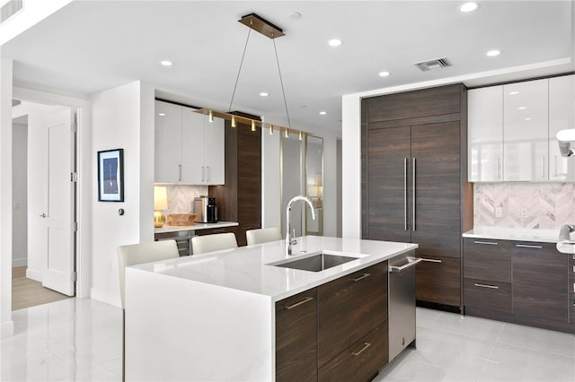 kitchen featuring sink, white cabinetry, hanging light fixtures, tasteful backsplash, and a center island with sink