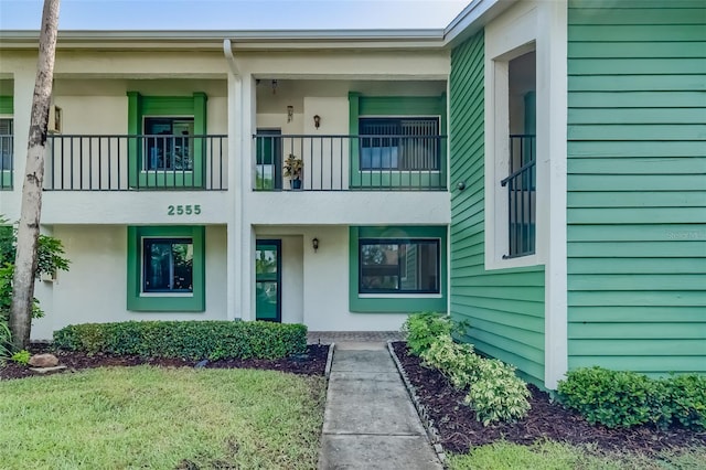 view of exterior entry featuring a balcony and a lawn