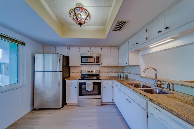 kitchen featuring appliances with stainless steel finishes, light hardwood / wood-style flooring, white cabinets, sink, and a tray ceiling