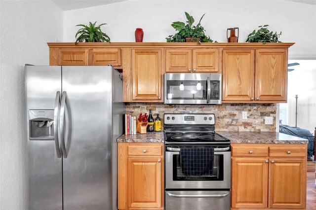 kitchen with appliances with stainless steel finishes, dark stone counters, tasteful backsplash, hardwood / wood-style floors, and lofted ceiling