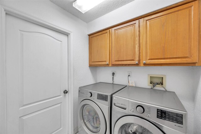 laundry area with washing machine and clothes dryer, a textured ceiling, and cabinets