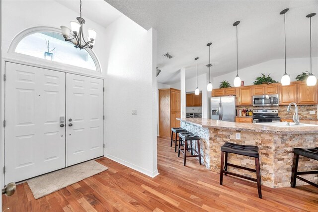 foyer entrance featuring high vaulted ceiling, light hardwood / wood-style flooring, sink, and an inviting chandelier