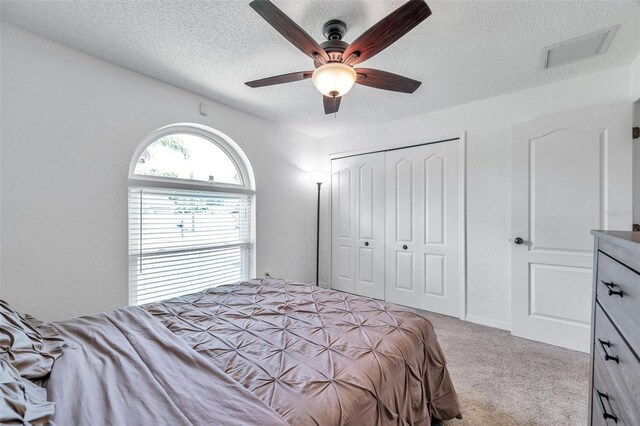 carpeted bedroom with a closet, a textured ceiling, and ceiling fan