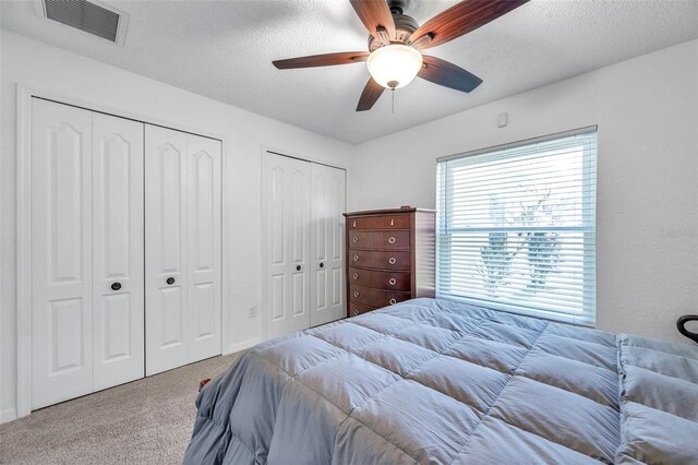 bedroom featuring light carpet, multiple closets, a textured ceiling, and ceiling fan