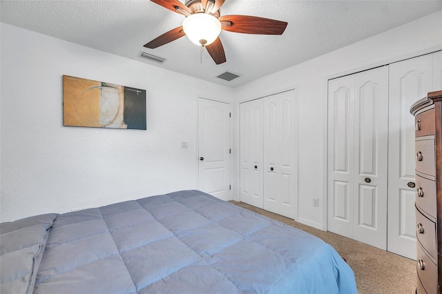 carpeted bedroom featuring multiple closets, a textured ceiling, and ceiling fan