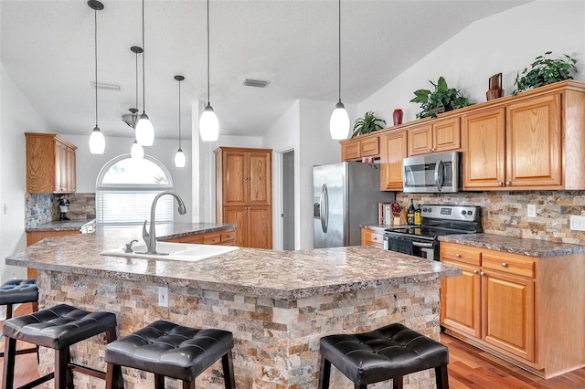 kitchen with lofted ceiling, light hardwood / wood-style flooring, appliances with stainless steel finishes, a large island with sink, and a kitchen bar