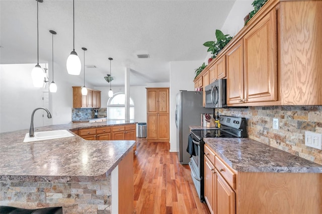 kitchen with kitchen peninsula, light hardwood / wood-style floors, appliances with stainless steel finishes, decorative backsplash, and sink