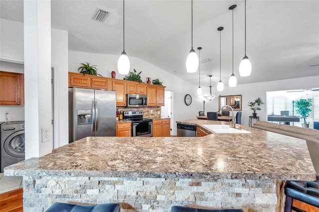 kitchen with a kitchen bar, appliances with stainless steel finishes, sink, washer / dryer, and a large island with sink