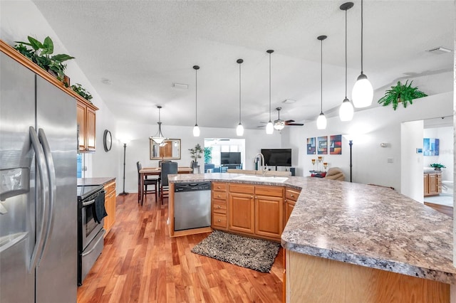 kitchen with decorative light fixtures, sink, appliances with stainless steel finishes, light hardwood / wood-style flooring, and a textured ceiling