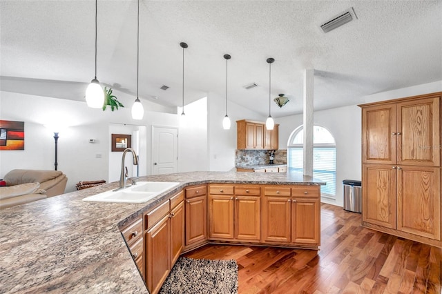 kitchen featuring sink, decorative light fixtures, hardwood / wood-style floors, and vaulted ceiling