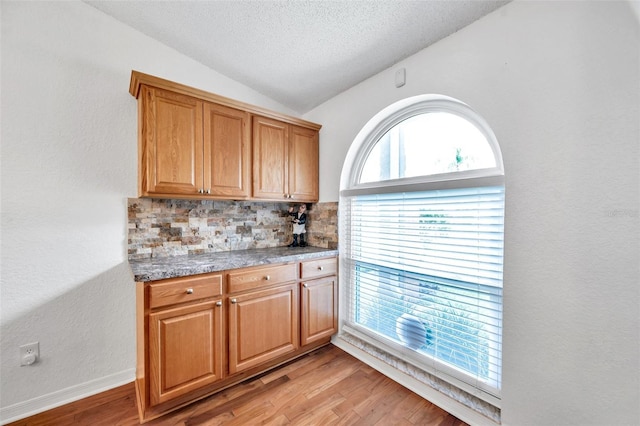 kitchen featuring a healthy amount of sunlight, light hardwood / wood-style floors, vaulted ceiling, and tasteful backsplash