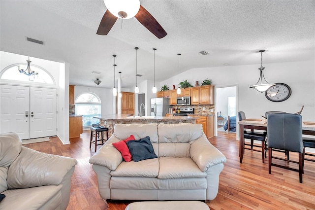 living room with light wood-type flooring, ceiling fan, lofted ceiling, and a textured ceiling