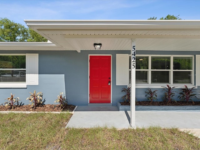 view of exterior entry with covered porch and a lawn