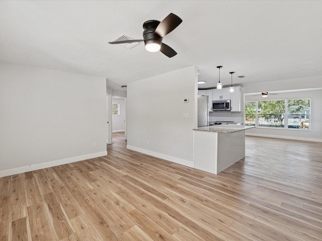 kitchen with appliances with stainless steel finishes, white cabinets, backsplash, hanging light fixtures, and light wood-type flooring