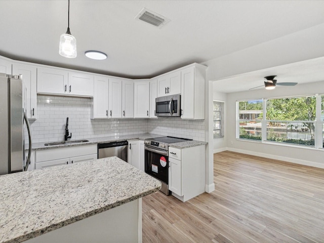 kitchen featuring appliances with stainless steel finishes, white cabinetry, sink, hanging light fixtures, and light stone counters