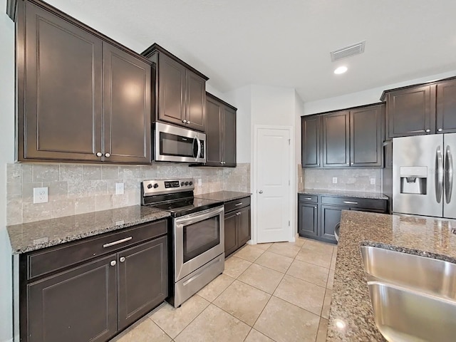 kitchen with dark brown cabinetry, stone countertops, visible vents, stainless steel appliances, and backsplash