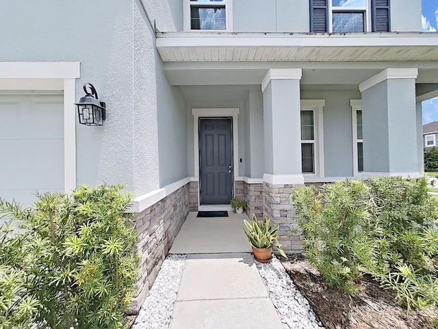 entrance to property featuring a porch, stone siding, and stucco siding