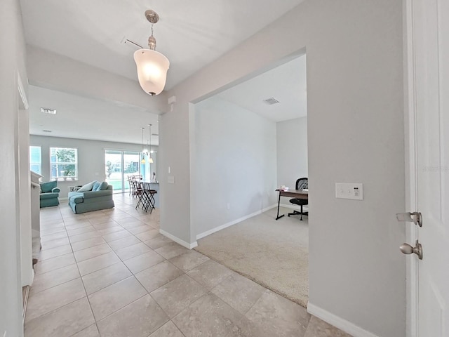 hallway featuring light colored carpet, visible vents, baseboards, and light tile patterned floors