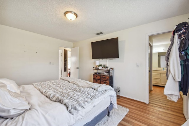 bedroom with light hardwood / wood-style floors, connected bathroom, and a textured ceiling