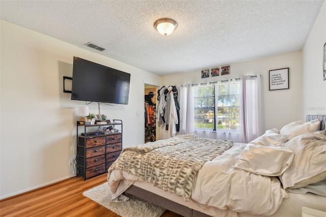 bedroom featuring a spacious closet, a closet, a textured ceiling, and hardwood / wood-style floors