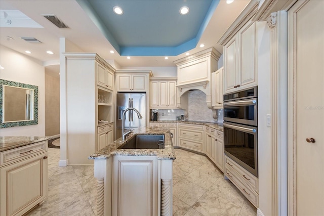 kitchen with stainless steel appliances, sink, a center island with sink, and cream cabinetry