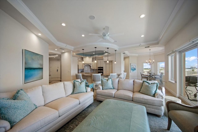 living room with a tray ceiling, crown molding, and ceiling fan with notable chandelier