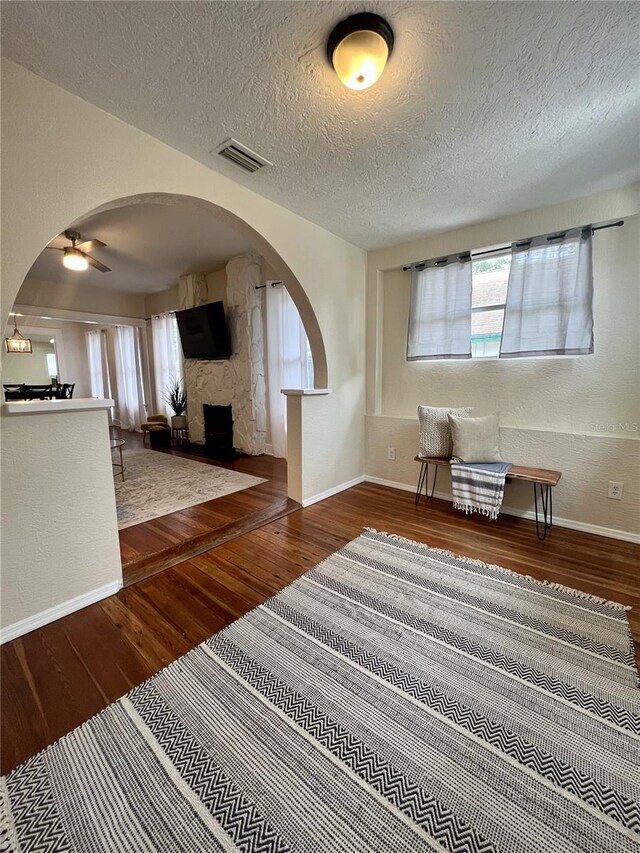 interior space with dark wood-type flooring, a textured ceiling, ceiling fan, and a stone fireplace