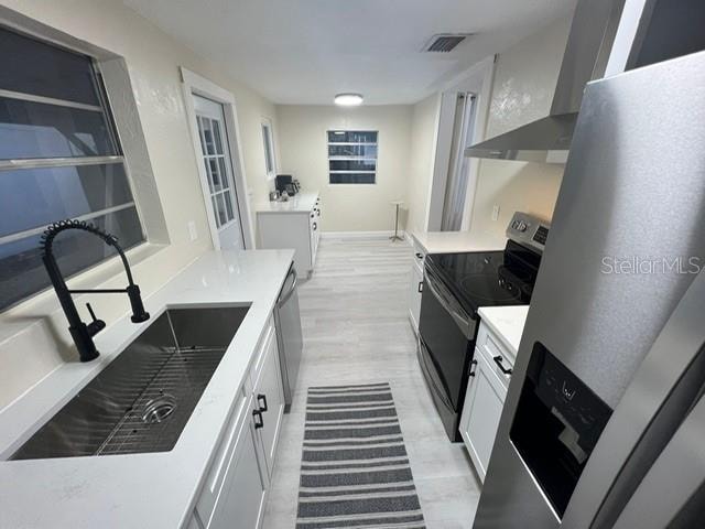 kitchen featuring sink, appliances with stainless steel finishes, white cabinetry, and wall chimney exhaust hood