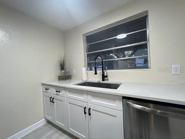 bar with light hardwood / wood-style flooring, white cabinets, sink, and stainless steel dishwasher