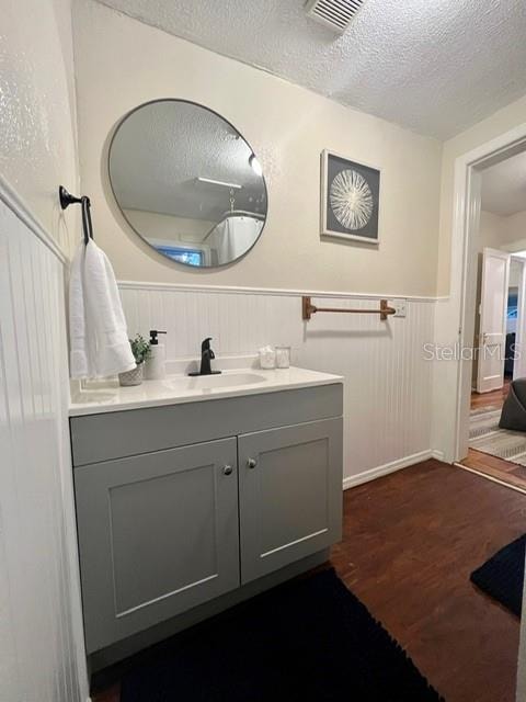 bathroom with a textured ceiling, vanity, hardwood / wood-style floors, and wooden walls