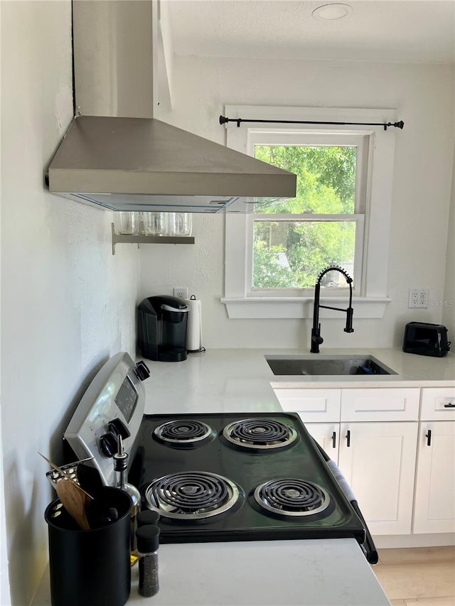 kitchen with light wood-type flooring, black range, white cabinetry, island range hood, and sink