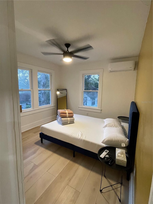 bedroom featuring ceiling fan, a wall mounted air conditioner, and light hardwood / wood-style floors