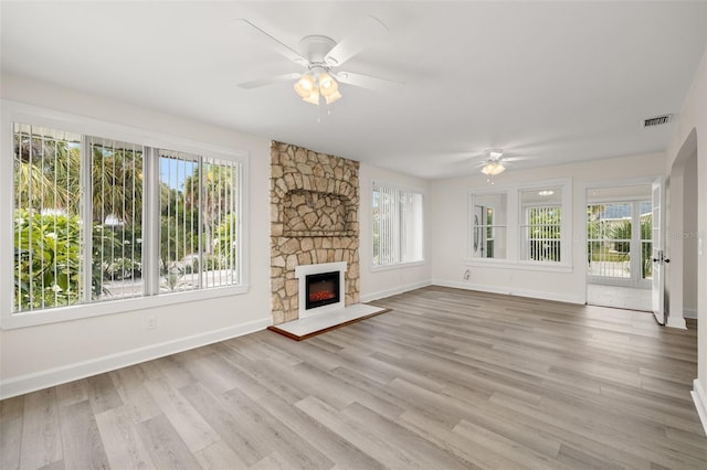 unfurnished living room featuring a stone fireplace, a wealth of natural light, light wood-type flooring, and ceiling fan