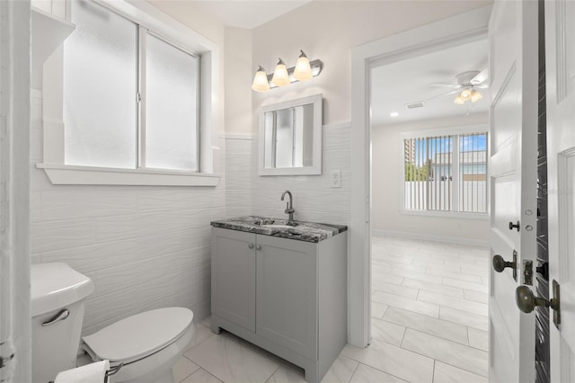 bathroom with toilet, vanity, ceiling fan, tile walls, and tile patterned floors