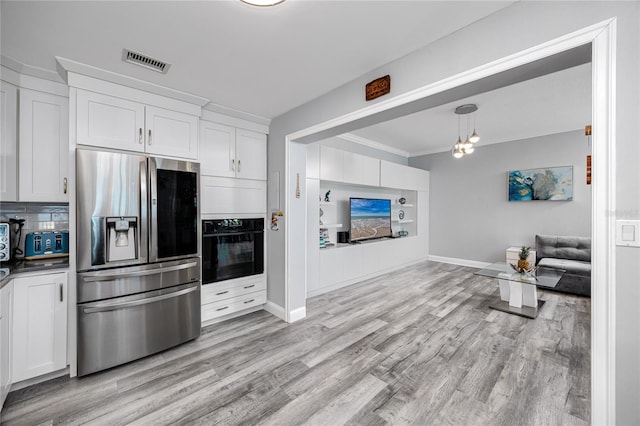 kitchen with stainless steel refrigerator with ice dispenser, visible vents, ornamental molding, white cabinets, and black oven