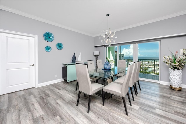 dining area with wood-type flooring, a water view, ornamental molding, and an inviting chandelier