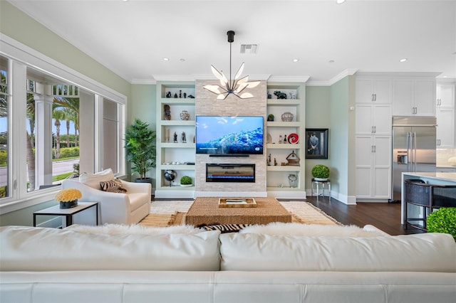 living room with dark wood-type flooring, a large fireplace, ornamental molding, built in features, and a notable chandelier