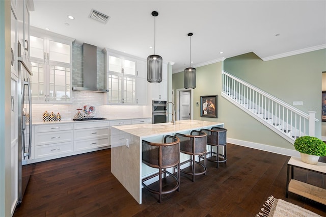 kitchen featuring a breakfast bar, white cabinetry, an island with sink, black electric cooktop, and wall chimney exhaust hood