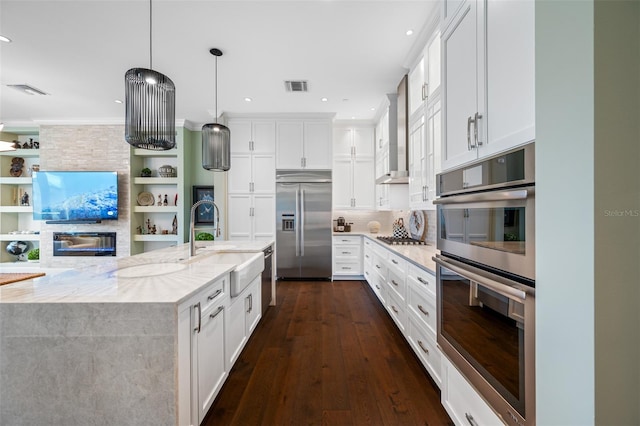 kitchen with appliances with stainless steel finishes, sink, white cabinets, light stone countertops, and wall chimney range hood