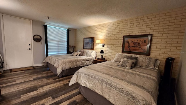 bedroom featuring dark wood-type flooring, brick wall, and a textured ceiling