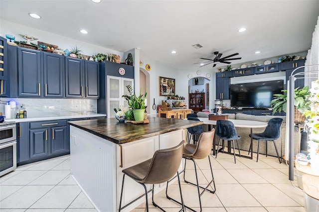 kitchen with light tile patterned floors, a breakfast bar area, backsplash, blue cabinets, and wood counters