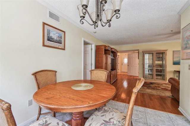 dining room featuring an inviting chandelier, ornamental molding, light hardwood / wood-style floors, and a textured ceiling