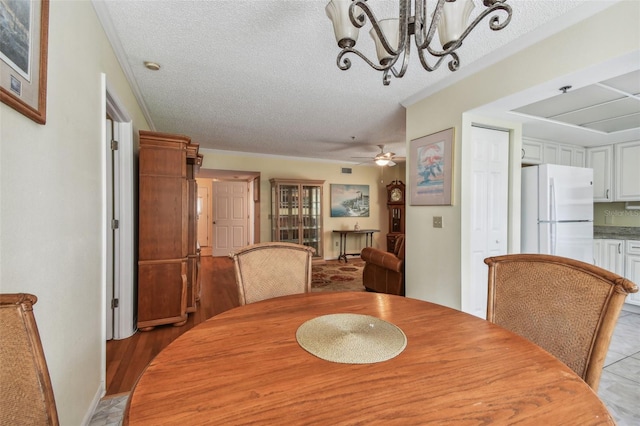 dining space featuring crown molding, ceiling fan with notable chandelier, and a textured ceiling