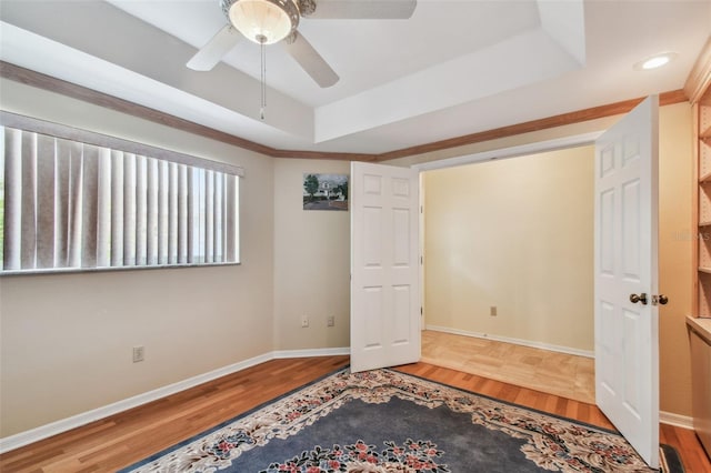 unfurnished bedroom with wood-type flooring, crown molding, ceiling fan, and a tray ceiling