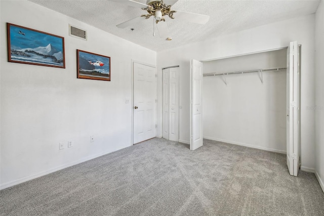 unfurnished bedroom featuring light colored carpet, two closets, a textured ceiling, and ceiling fan